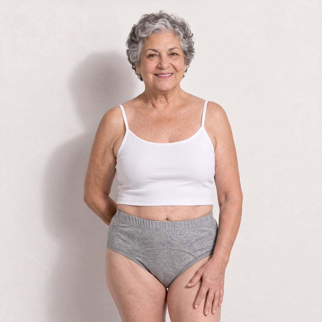 Femme aux cheveux gris bouclés portant la culotte grise Urikare de face avec un petit haut blanc.