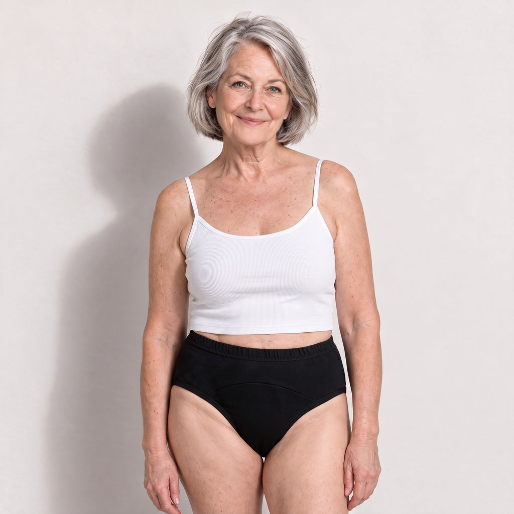 Femme aux cheveux gris portant la culotte noire Urikare de face avec un petit haut blanc.